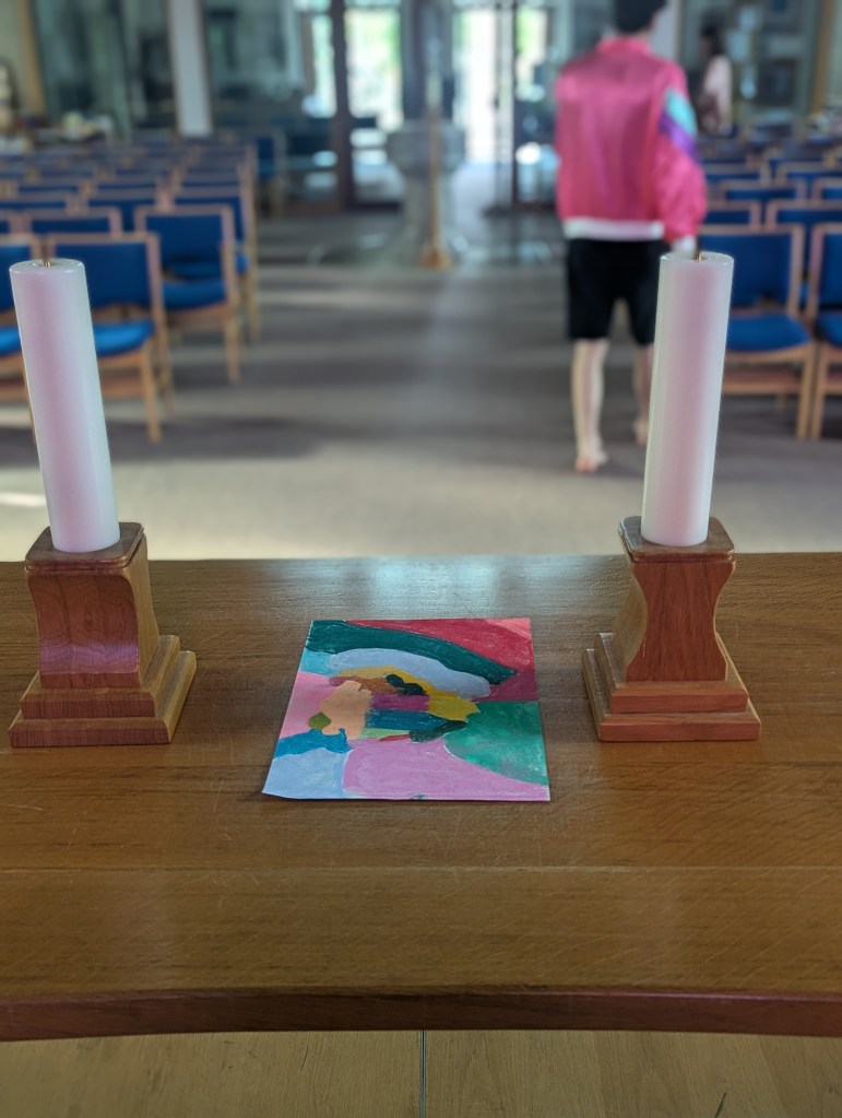 A multi-coloured drawing in pastels on a table, in between two candles in the church.